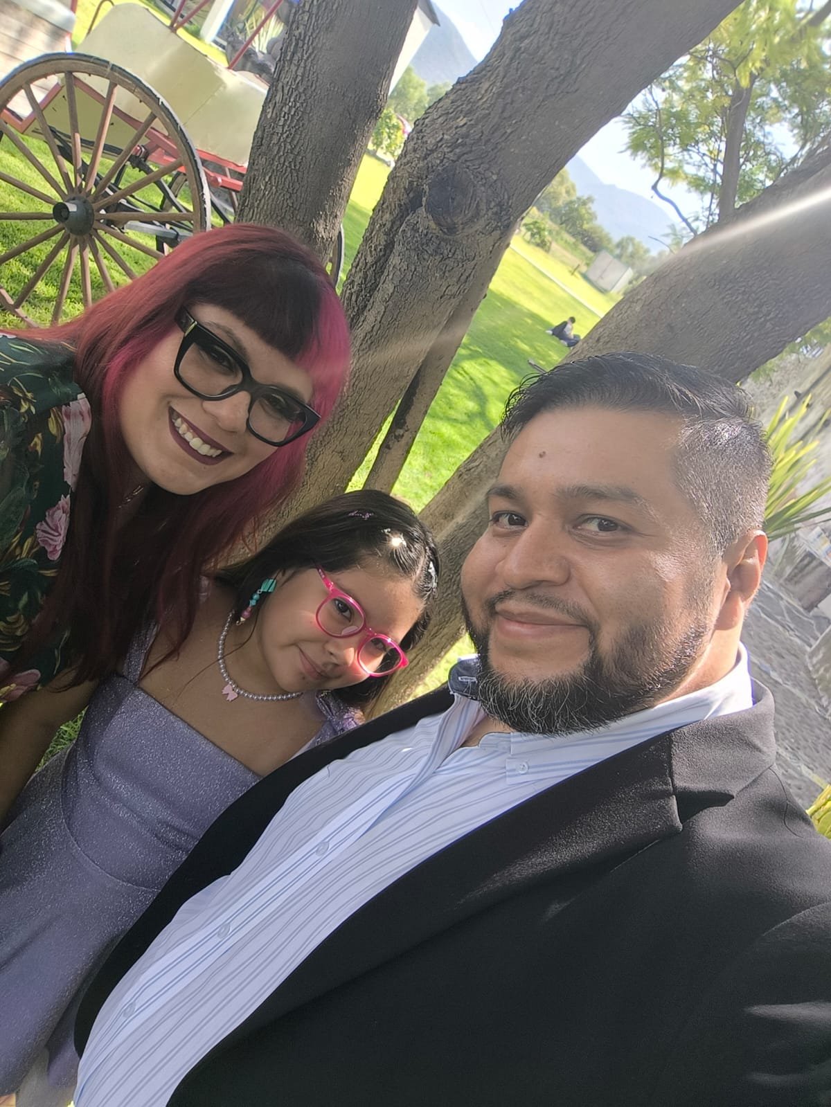 Ana Belen con su familia, sonriendo junto a un árbol en un día soleado